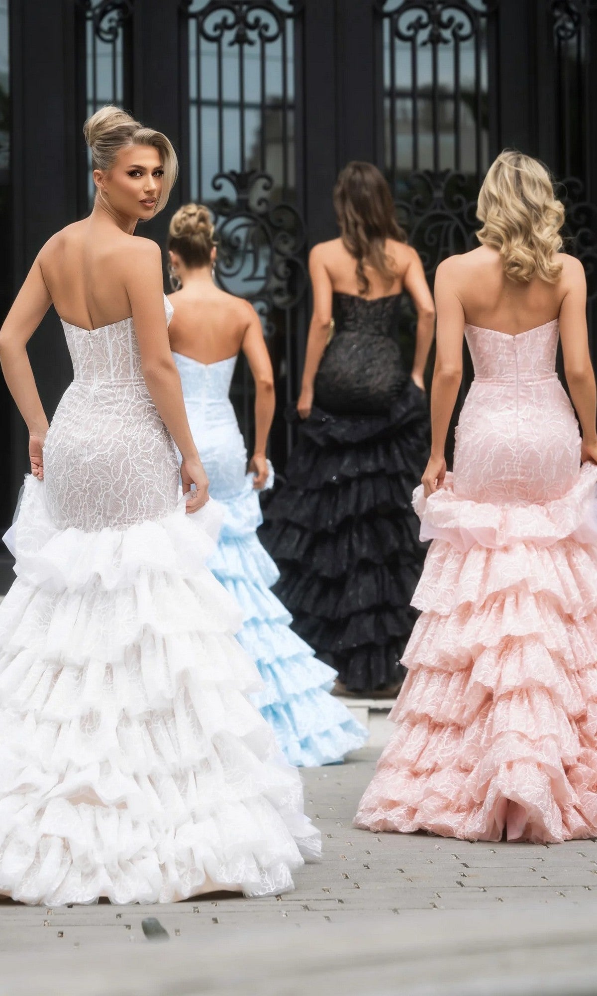 Four women wearing Portia and Scarlett PS25250 long formal dresses with strapless boned corset bodices and ruffled tiered skirts walk away from the camera.